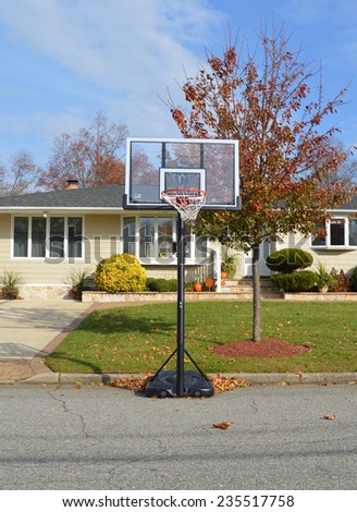 Basketball hoop on street in front of Suburban ranch home autumn day tree residential neighborhood blue sky clouds USA