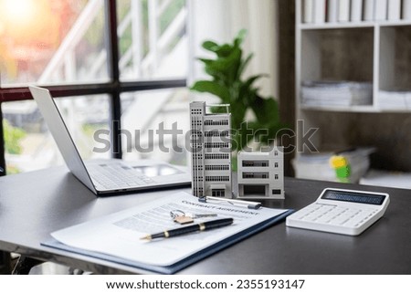 Wooden table with laptop, house keys Clipboard with pen, house model and green tree calculator, real estate concept. close up pictures