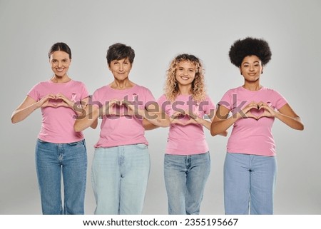 breast cancer awareness, happy interracial women with pink ribbons showing heart on grey, diversity Royalty-Free Stock Photo #2355195667