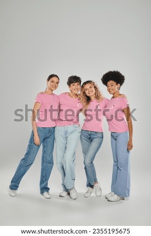 breast cancer awareness, cheerful multicultural women with pink ribbons hugging on grey, diversity Royalty-Free Stock Photo #2355195675