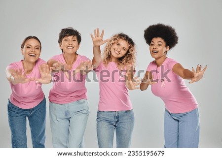 breast cancer awareness, joyful interracial women with pink ribbons on grey, diversity, cancer free