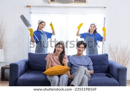 Asian newlywed business people decide to choose professional cleaning service teamwork to clean and tidy up new house, both housekeeper team husband and wife happy sitting on sofa at home thumbs up