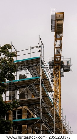 A tall yellow tower crane positioned atop a large construction building, providing an efficient and reliable source of lifting and hoisting services