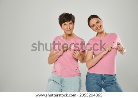 women touching pink ribbons, smiling, grey backdrop, different generations, breast cancer awareness Royalty-Free Stock Photo #2355204865
