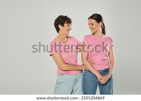 women with pink ribbons smiling, grey backdrop, hug, different generations, breast cancer awareness Royalty-Free Stock Photo #2355204869