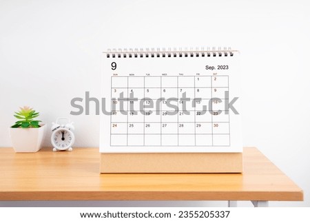 September 2023, Monthly desk calendar for 2023 year on wooden table with alarm clock.