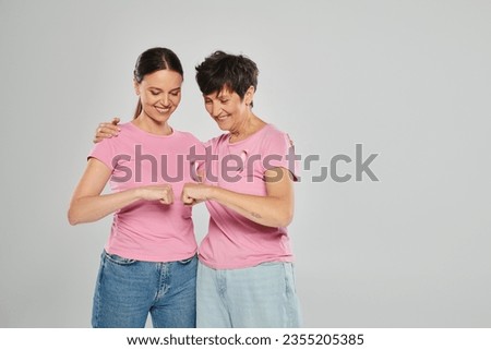 breast cancer concept, happy women with pink ribbons fist bumping on grey backdrop, cancer free Royalty-Free Stock Photo #2355205385