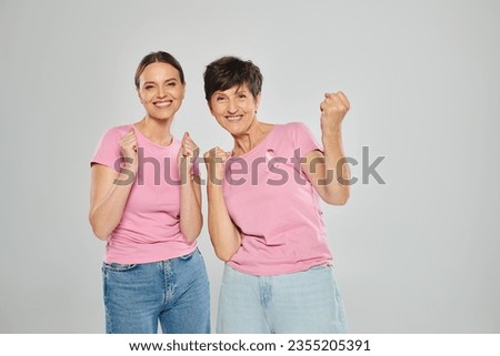 breast cancer concept, excited women looking at camera and gesturing on grey backdrop, yes, yay Royalty-Free Stock Photo #2355205391