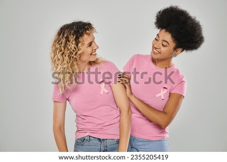 breast cancer awareness, cheerful multicultural women with pink ribbons on grey backdrop, diversity Royalty-Free Stock Photo #2355205419