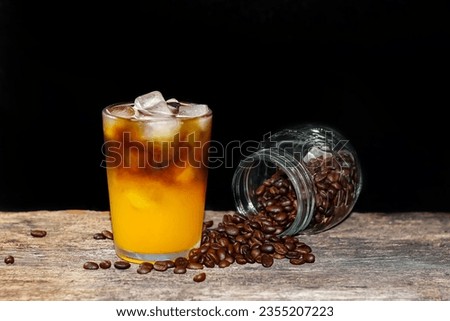 Americano ice coffee and coffee beans spread on the old wooden with closeup photo in darkness background.