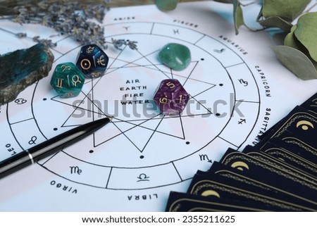 Zodiac wheel with sign triplicities, pen, tarot cards, gemstones and astrology dices on table, closeup