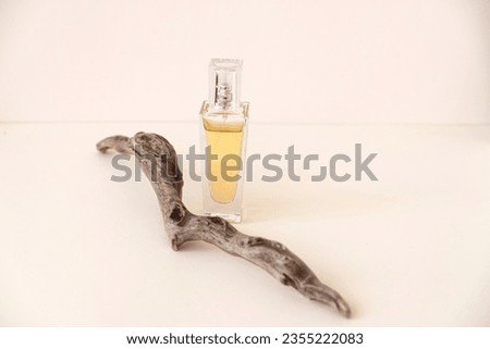 A composition of yellow perfume bottle balancing on beige color stone and a twig of driftwood.