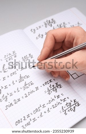 Woman writing maths formulas in copybook with pencil, closeup