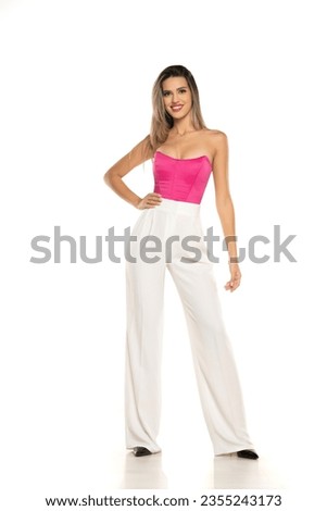 young modern smiling woman in white pants and pink corset posing on white studio background