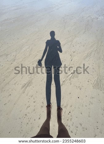 A woman Shawdow standing barefoot on a sand beach.
