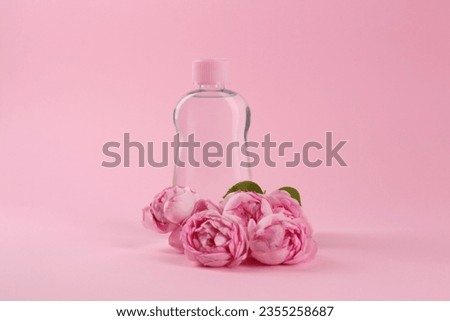 Bottle with baby oil and beautiful flowers on pink background. Space for text