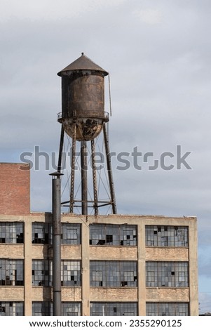 Abandoned automotive factory with broken windows and a water tower. Abandoned factories are dangerous and eyesores. Royalty-Free Stock Photo #2355290125