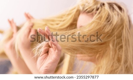 Haircare, health problem concept. Unhappy sad woman looking at damaged split ends on her blonde hair. Female in bathroom next to mirror.