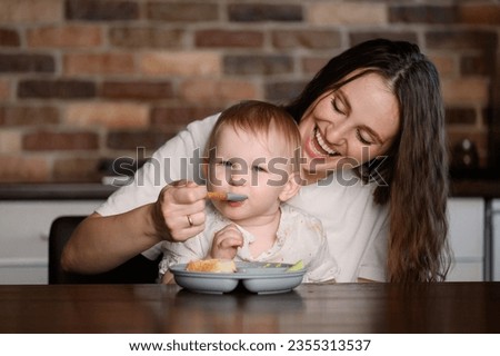 Mom holds a child in her arms, feeds a happy kid with healthy food with a spoon. Healthy food.Complementary feeding