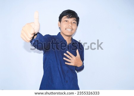 proud young asian man smiling with grateful face for survived from heart attack and has recovery is holding chest with thunbs up wearing navy shirt