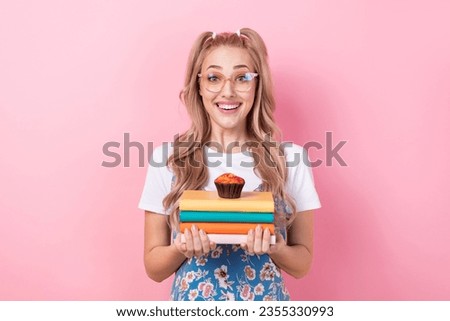 Photo of cheerful adorable person toothy smile hands hold pile stack book muffin dessert isolated on pink color background