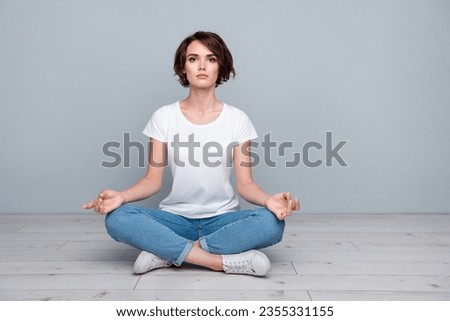 Full length photo of focused girl wear stylish t-shirt sitting on floor in meditation pose focusing isolated on gray color background