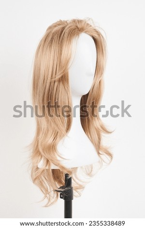 Natural looking blonde wig on white mannequin head. Long hair on the plastic wig holder isolated on white background
