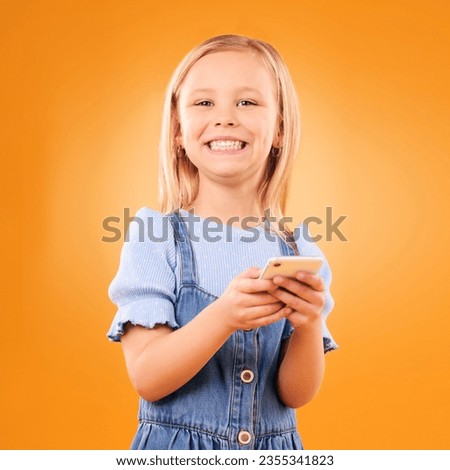 Child, portrait and typing with smartphone in studio for social media, play mobile games and smile on orange background. Happy girl kid, phone and reading notification, watch multimedia and tech app