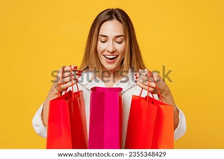 Young surprised fun cool woman wear white casual clothes hold in hand open paper package bags after shopping look camera isolated on plain yellow background studio. Black Friday sale buy day concept
