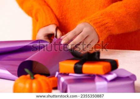 Woman wrapping gift boxes for Halloween at white table Royalty-Free Stock Photo #2355350887