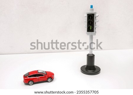a red toy car stands in front of a traffic light with a green signal.