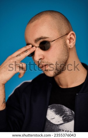 Studio shot of a young tattoed bald man posing against a blue background. 90s style.