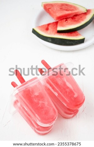 Closeup of homemade watermelon popsicles in their mold with watermelon slices, white background, vertical, with copy space