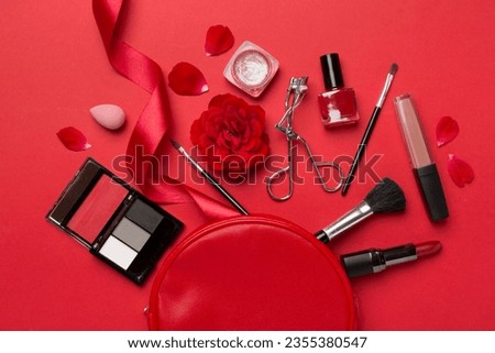 Cosmetic bag with makeup products and flowers on color background