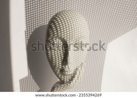A checkered shadow falls on a statuette with the face of a young girl on her arm on a white background.