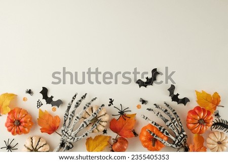 Delighting in the strange and captivating allure of Halloween. Top view shot of scary skeleton hands, pumpkins, autumn leaves, halloween decor on light grey background with advertising zone