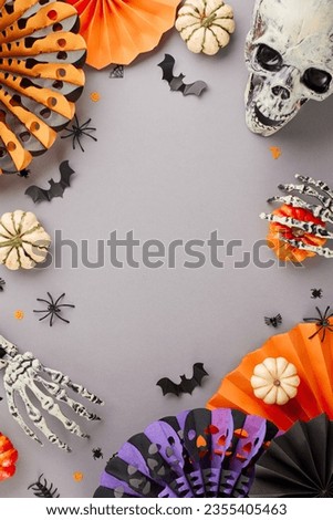 Get in the Halloween spirit. Top view vertical shot of paper party props, skull, scary skeleton hands, pumpkins, spooky decorations on grey background with advertisement area