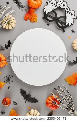 Halloween festivity idea. Top view vertical photo of ghostly eyewear, skeleton hands, pumpkins, autumn leaves, sinister insects on grey background with blank circle for advert or text