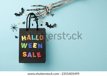 Happy Halloween discounts in stores. Top view arrangement of a package with a halloween sale inscription, creepy skeleton hand, scary decor on light blue background with commercial placeholder