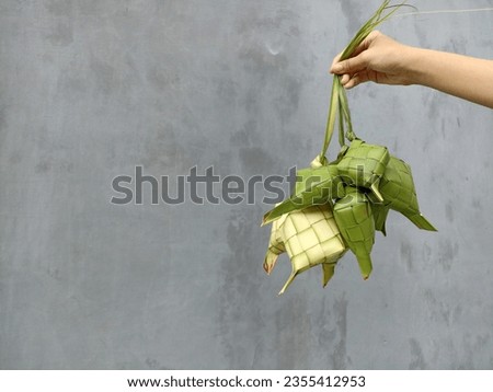 Ketupat (Rice Dumpling) in hand on gray wall background. Ketupat is a natural rice casing made from young coconut leaves for cooking rice during eid Mubarak. Copy space for text card design. 