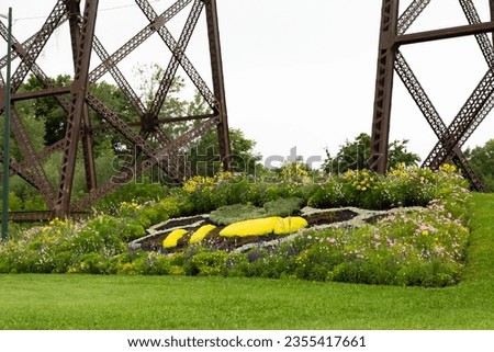 Landscaping in the shape of a bee surrounded by flowers in central median, with part of the 1908 railway trestle bridge in the background, Cap-Rouge area, Quebec City, Quebec, Canada Royalty-Free Stock Photo #2355417661