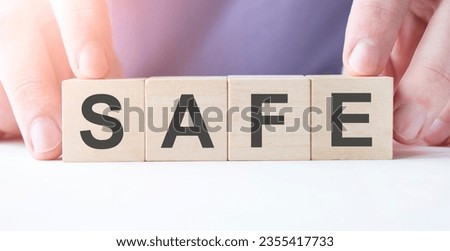 Businessman hand holding wooden cube block with SAFE business word on table background.