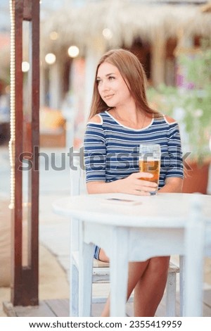 Portrait of a young woman drinking beer on the terrace of a beach cafe on a summer sunny day