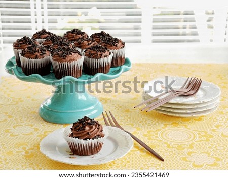 Mini chocolate cupcakes on turquoise cakestand  with small plates and rose gold forks on yellow patterned tablecloth in horizontal format with selective focus on front cupcake.
 Royalty-Free Stock Photo #2355421469