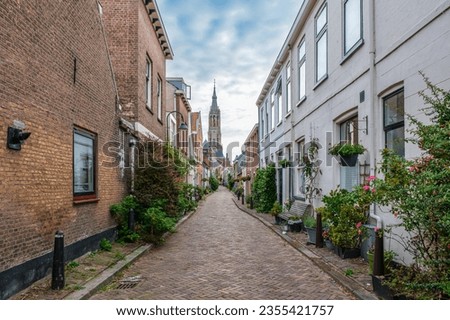 Picturesque Delft cityscape with a view through a narrow ancient alley on the tower of the famous Nieuwe Kerk. Delft, the Netherlands. Old alley is called Trumpet Street Royalty-Free Stock Photo #2355421757