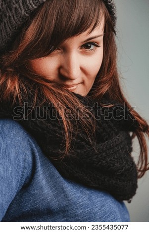Donning winter gear, a spirited woman feigns a grumpy look, but her eyes gleam with joy. She's dressed warmly in woolen essentials, with her brown locks flowing and eyes full of life Royalty-Free Stock Photo #2355435077