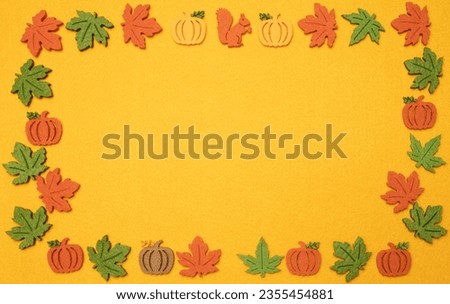 funny multi-colored felt parts in the form of pumpkins, autumn maple leaves are laid out in the form of a frame on a yellow felt background.