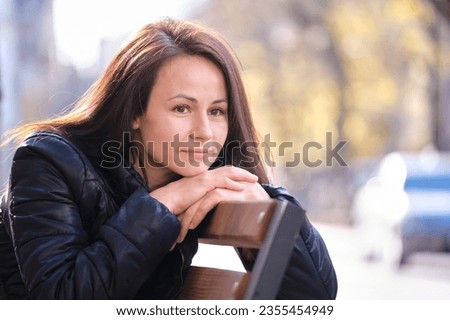 Young sad woman sitting alone on street bench outdoors thinking about something. Loneliness and depression during hard period in life concept