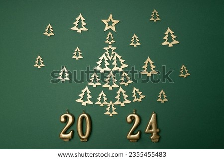 wooden decorations in gold color in the form of Christmas trees are laid out in the form of a Christmas tree on a green background with candles 2024. The concept of the New Year.