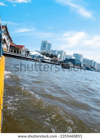 This picture shows a view of a city from a boat on a river. The river is brown and has waves on its surface.